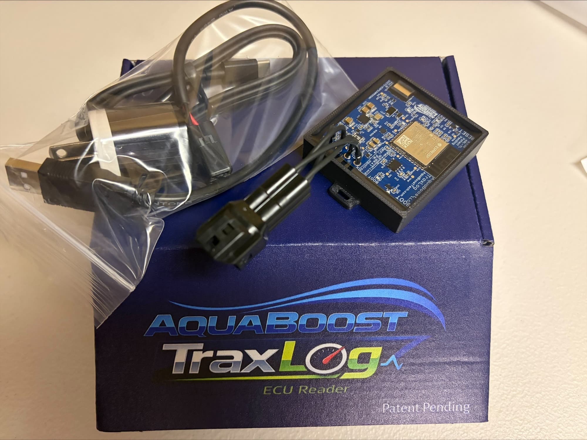 An AquaBoost TraxLog kit on its branded box — the module with its DLC harness, the USB-C cable, and the power block